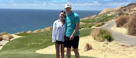 Una pareja está de pie en un campo de golf con vista al océano.