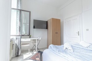 A bedroom with a bed, a desk, a wardrobe, and a television.