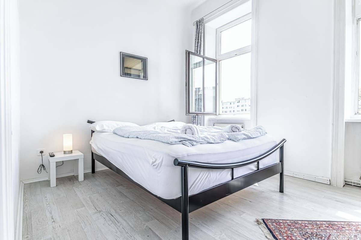 A modern bedroom with a bed, bedside table, and a window with a view of buildings.