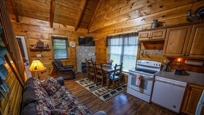 Interior acogedor de una cabaña con detalles de madera, una chimenea de piedra, una zona de comedor y una kitchenette.