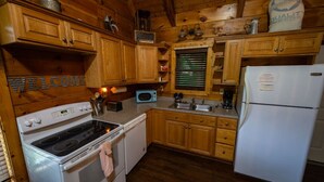 Una cocina tipo cabaña de madera con estufa, microondas, fregadero y refrigerador.