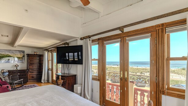 Une chambre dotée d’un grand lit, d’une armoire en bois, d’une télévision et d’un balcon offrant une vue sur la plage.