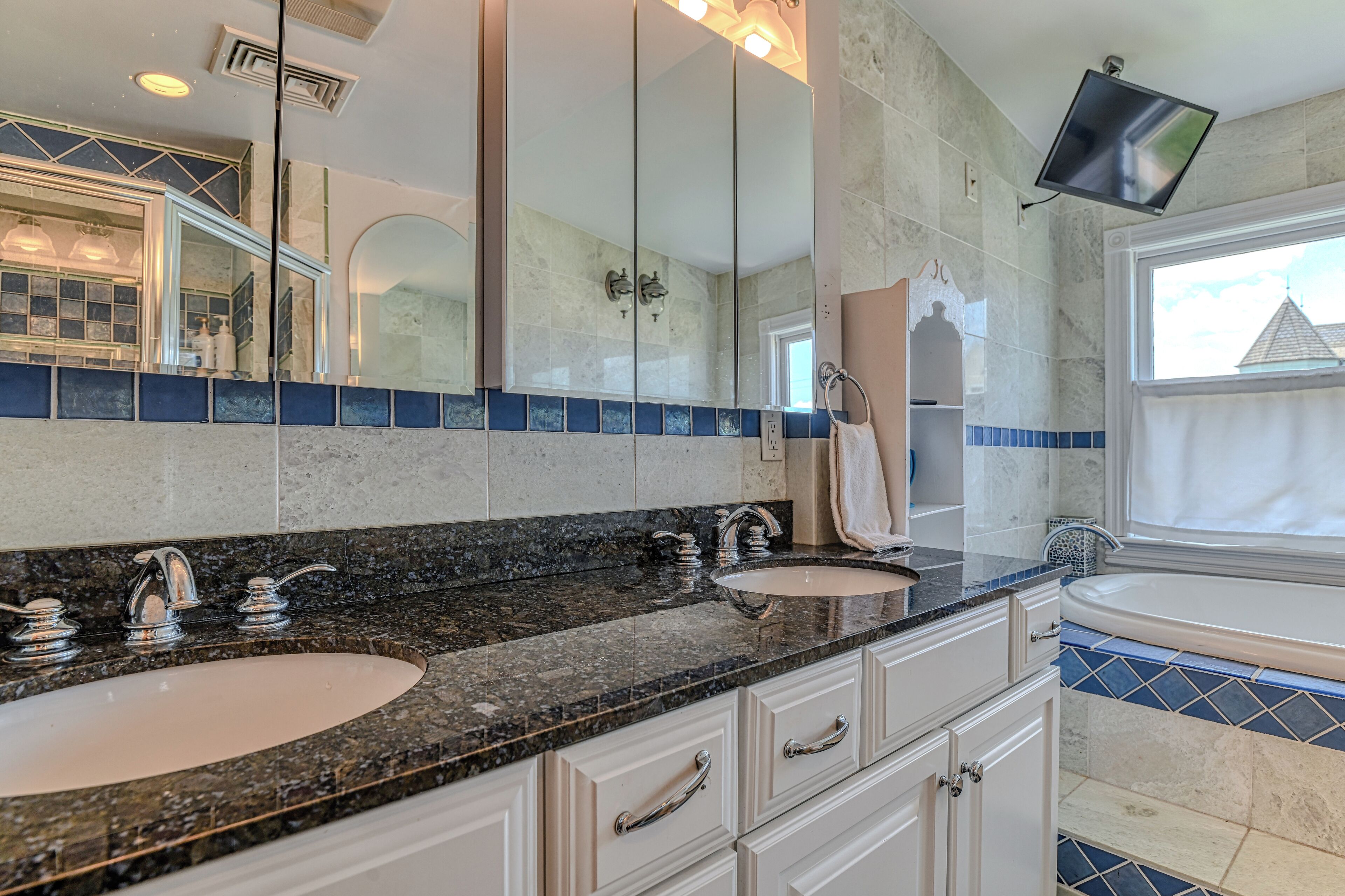 Une salle de bain avec deux lavabos, un grand miroir, un téléviseur fixé au mur et une baignoire.
