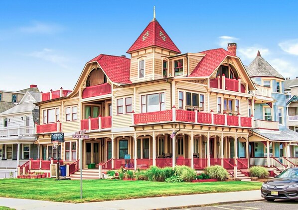 A large, multi-story building with a prominent red roof and multiple balconies. - Panoramic View Ocean Front Victorian House (Neptune Township)