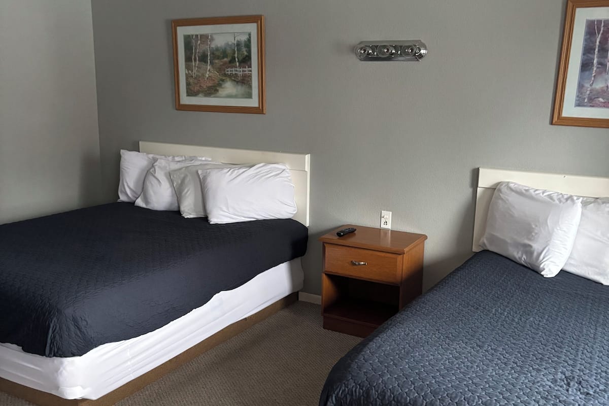 A hotel room with two beds, a nightstand, and a wall-mounted thermostat.