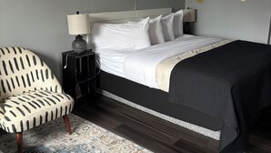 Ein ordentlich eingerichtetes Schlafzimmer mit Bett, Stuhl, Nachttisch, Lampe und einer Wandregal.
