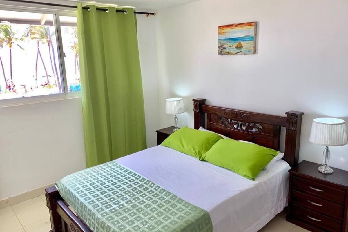 Una cama bien hecha con una colcha estampada, dos lámparas de noche y un cuadro en la pared.