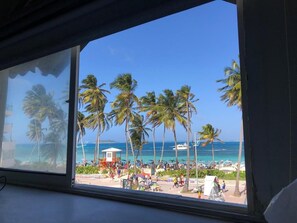 A beach view from inside a building with palm trees and a clear sky. - Apartamentos Beach Vista al Mar (San Andrés)