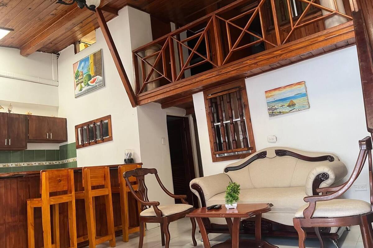 Amplia sala de estar con techo alto, muebles de madera y vista a la cocina.