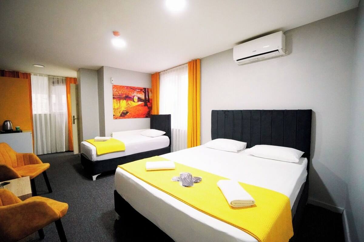 A hotel room with two beds, a desk, and an air conditioning unit.