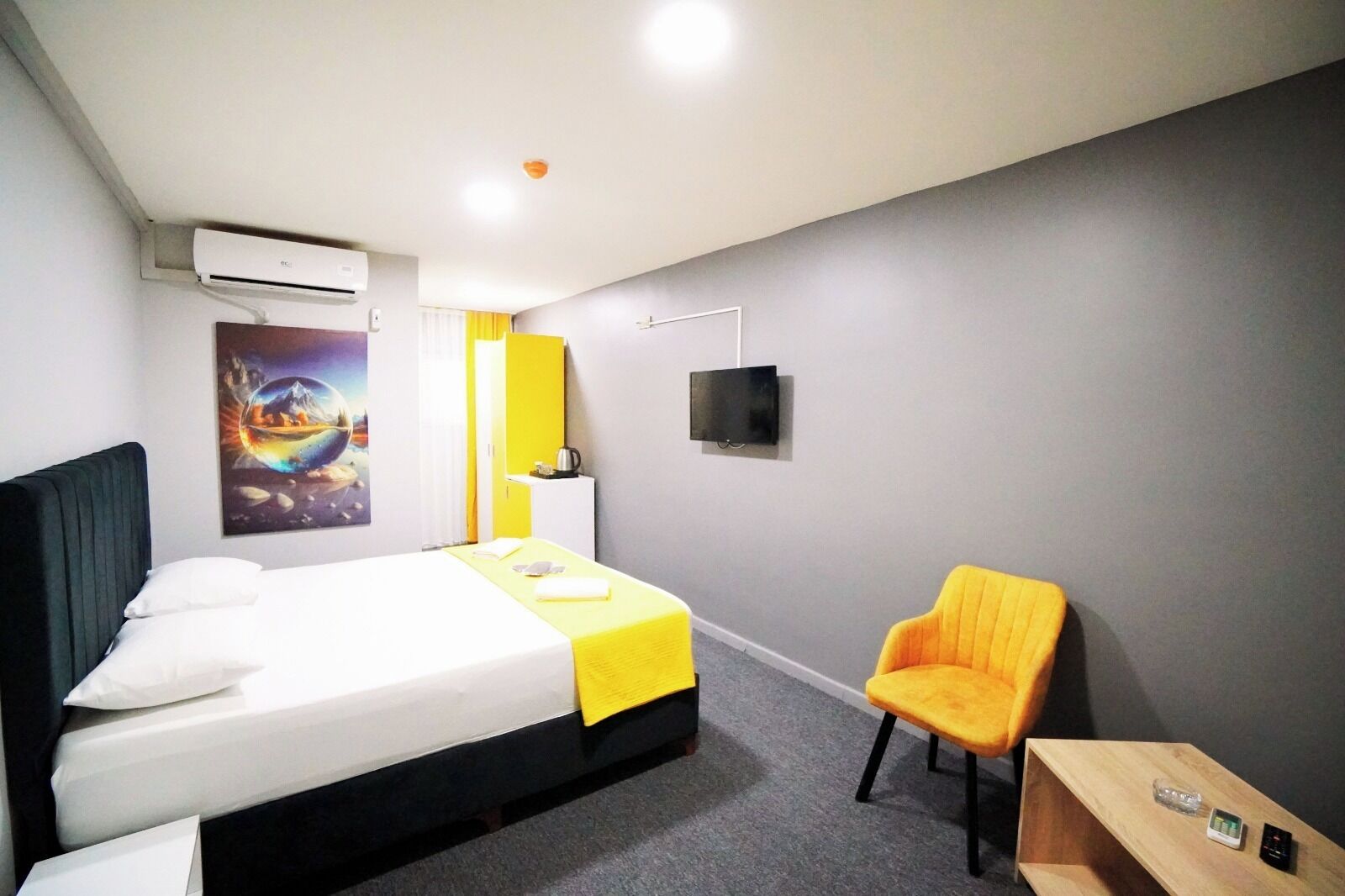 A hotel room with a bed, a chair, a TV, and an air conditioning unit.