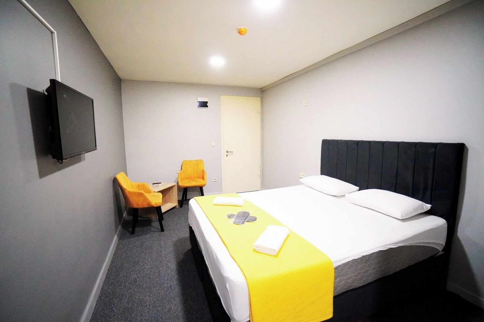 Ein Hotelzimmer mit einem Bett, einem Schreibtisch, zwei Sesseln, einem Fernseher und einer Tür.