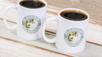 Deux tasses à café blanches ornées d’un motif tropical et d’une inscription, posées sur une surface en bois.