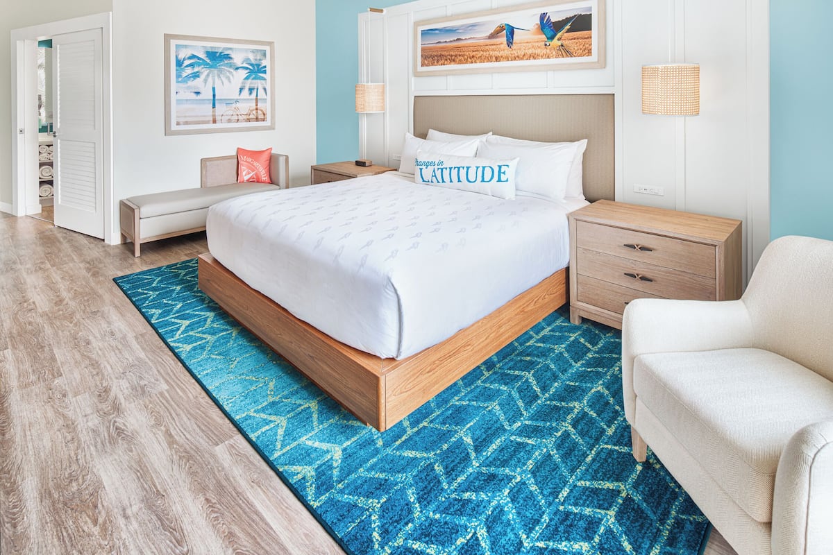 Un dormitorio con cama, mesitas de noche, una silla, un tapete azul estampado y obras de arte en las paredes.