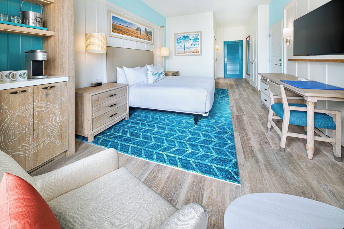 Una habitación de hotel con cama, escritorio, televisión, cafetera y baño.