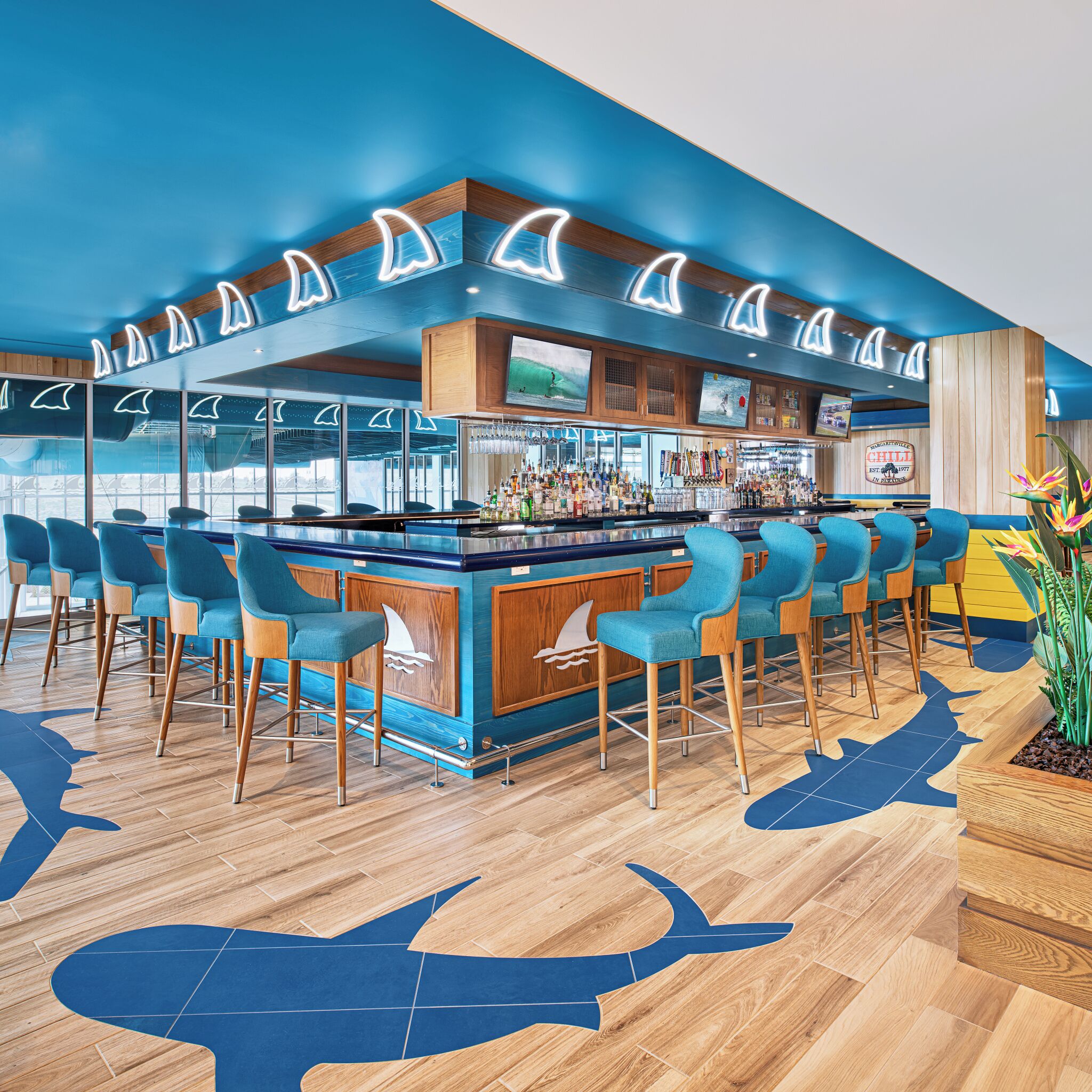 A bar area with wooden accents, blue chairs, and a nautical theme with shark silhouettes on the floor.
