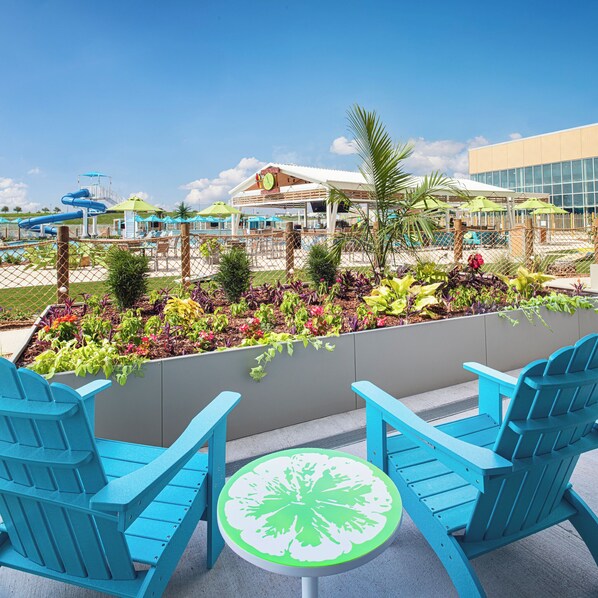 A poolside area with blue Adirondack chairs, a small round table, and a water slide in the background.