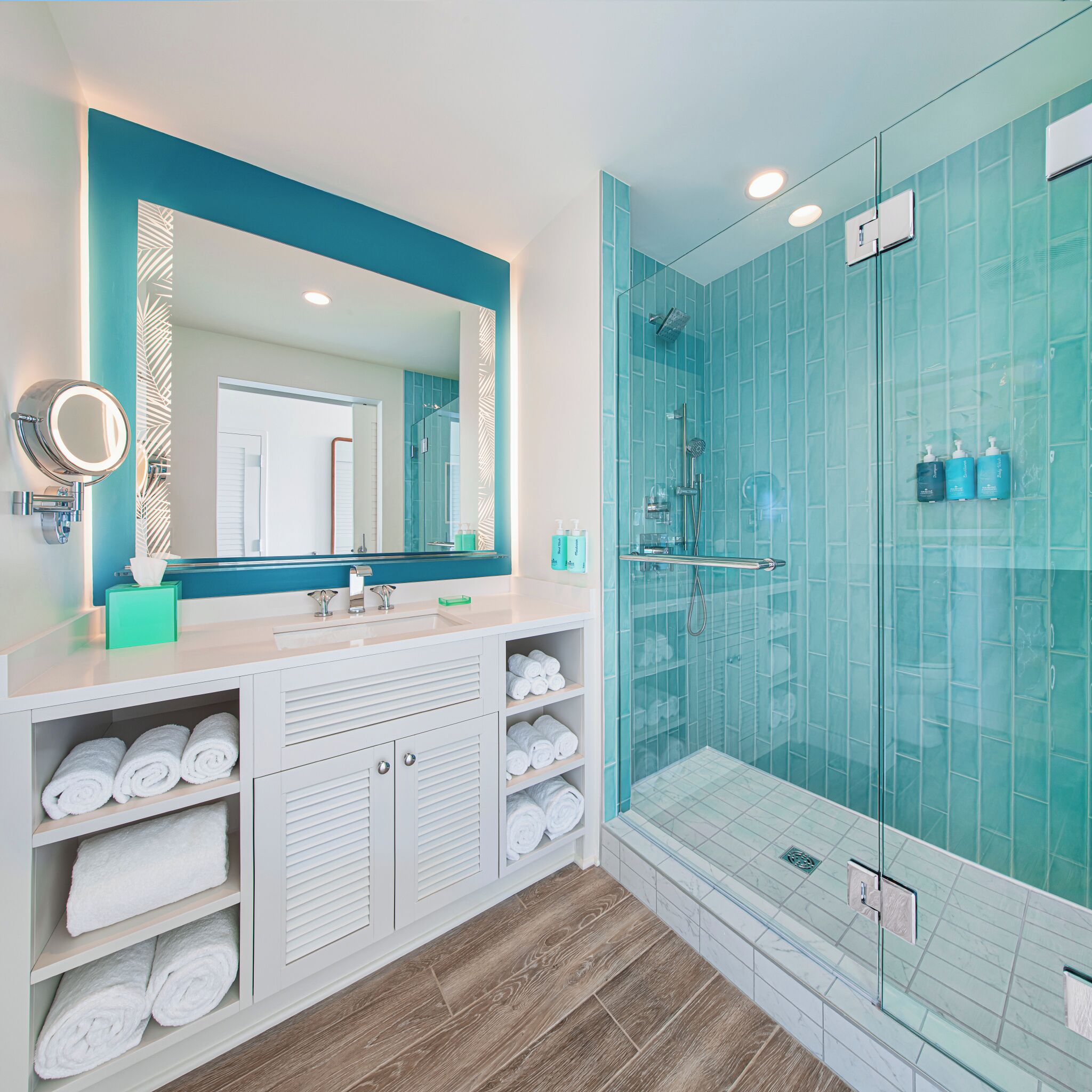 Un baño moderno con un espejo grande, cabina de ducha de vidrio y toallas ordenadas en estantes.
