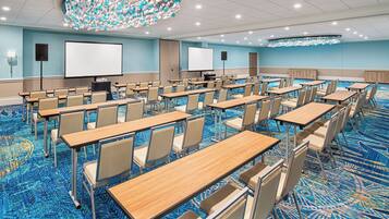 A conference room with rows of tables and chairs, a large screen, and a ceiling light fixture.