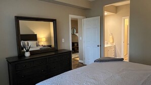 Une chambre à coucher avec un grand lit, une commode, un miroir et une porte donnant sur une salle de bain.