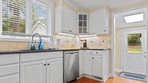 A kitchen with white cabinets, a dishwasher, and a window with blinds. - Downtown Village of Pinehurst 2BR/2BA (Pinehurst)