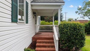 A white house with green shutters, a covered porch, and a brick staircase leading to the entrance. - Downtown Village of Pinehurst 2BR/2BA (Pinehurst)