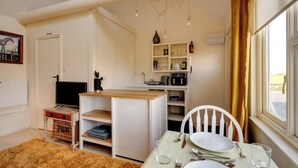 A compact kitchen with a dining area, a television, and a small storage unit. - Cosy and Equipped, Pvt Garden, Direct Access to Public Footpath, Dog Friendly. (Winston)