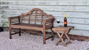 A wooden bench and a small table with a bottle of wine and a glass. - Cosy and Equipped, Pvt Garden, Direct Access to Public Footpath, Dog Friendly. (Winston)