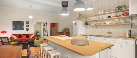 A modern kitchen with a wooden island, bar stools, pendant lights, and white cabinetry.