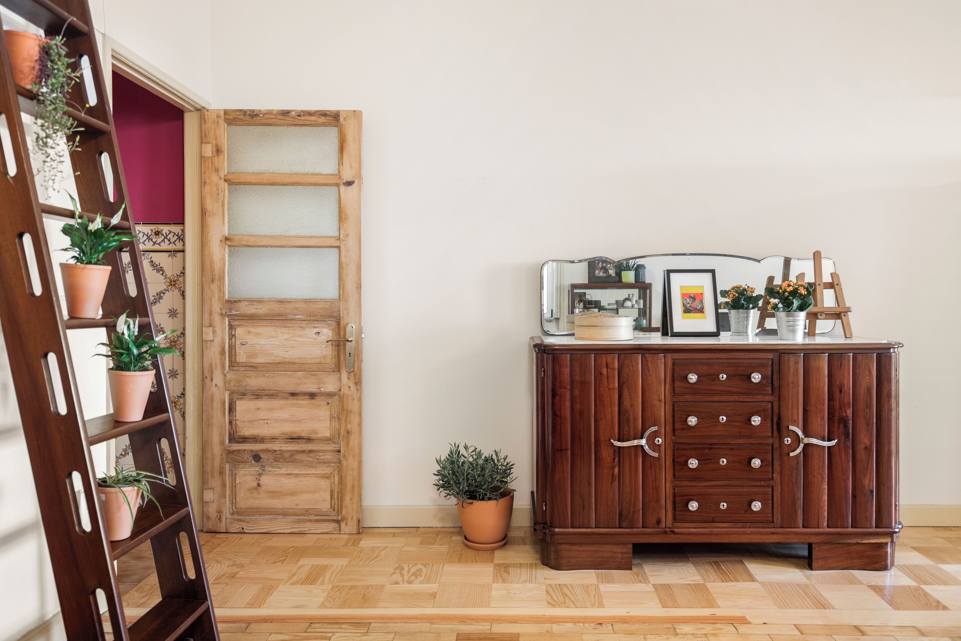 A wooden cabinet with drawers, a small potted plant, and a ladder with potted plants against a wall.
