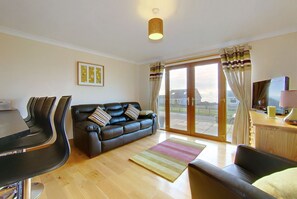 Un salon avec un canapé en cuir, une table basse en bois et un téléviseur posé sur un meuble en bois.
