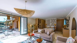 A spacious living area with a large sofa, coffee table, and a dining table. There is a balcony with outdoor seating and a view of the landscape. - To complete (Marrakech-Safi)