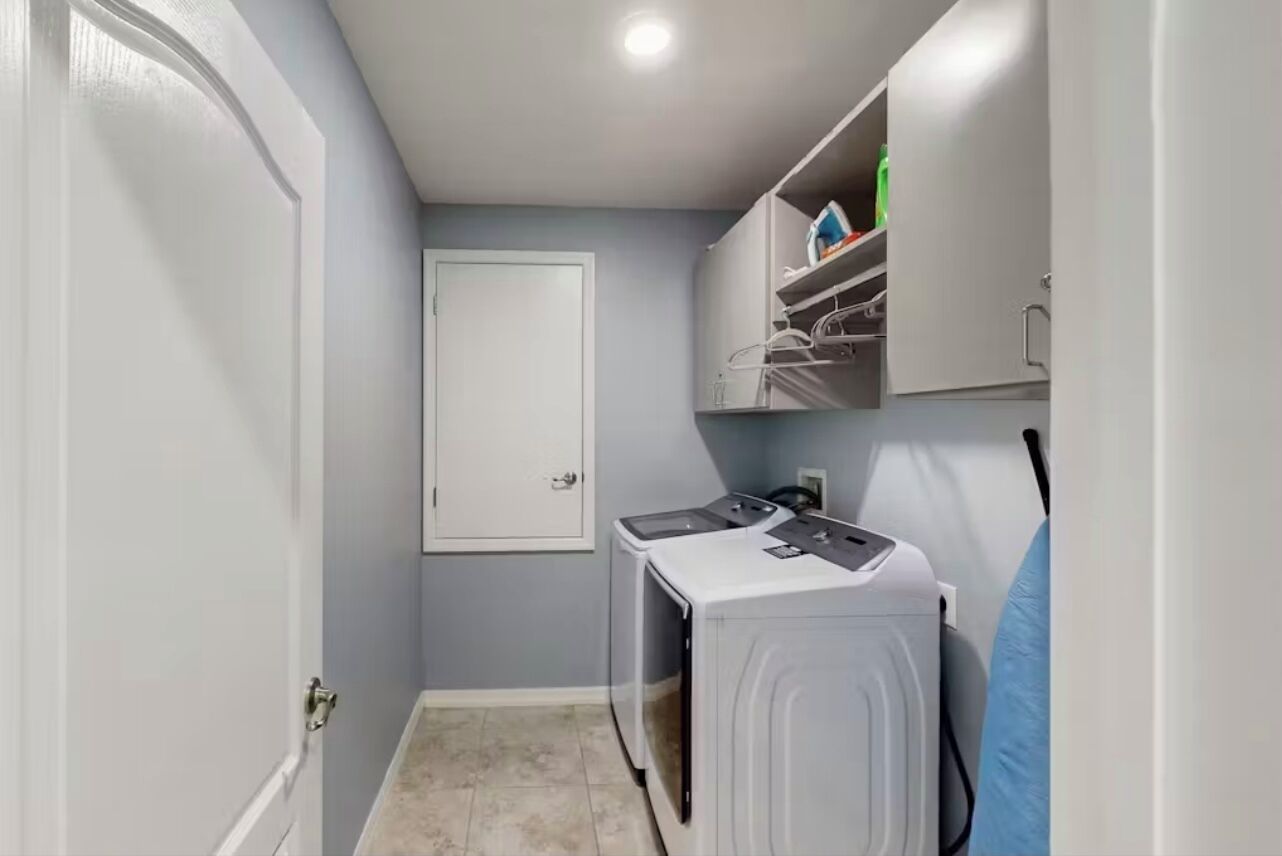 A laundry room with a washing machine, dryer, and shelving unit.