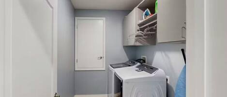 A laundry room with a washing machine, dryer, and shelving unit.