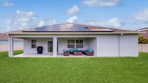 A modern single-story house with a covered patio area, solar panels on the roof, and a well-maintained lawn.