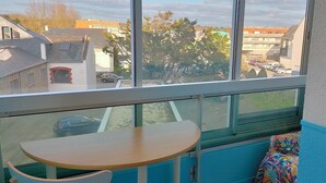 Une pièce avec une grande fenêtre, une petite table et un coussin aux couleurs vives.