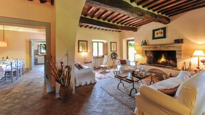 A spacious living room with a fireplace, wooden beams, and a dining area with a table set for four. - Stunning villa with large pool in the heart of Chianti 12km from Siena (Radda in Chianti)