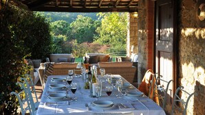 An outdoor dining area with a table set for a meal, surrounded by wicker furniture and a stone wall. - Stunning villa with large pool in the heart of Chianti 12km from Siena (Radda in Chianti)