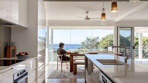 Eine moderne Küche mit einem großen Fenster mit Blick auf das Meer, einem Essbereich und einem Blick auf den Ozean.