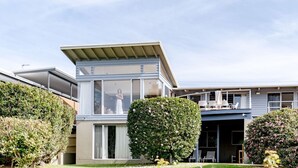 A modern two-story house with a flat roof, large windows, and a balcony with outdoor seating. - Everlong Mollymook - Spacious Home on Beachside Golf Course with Ocean views (Mollymook)