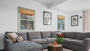 A living room with a grey sofa, a round wooden coffee table, and a framed artwork above the sofa.