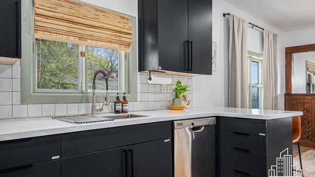 A modern kitchen with black cabinets, a stainless steel dishwasher, and a window with a bamboo blind.