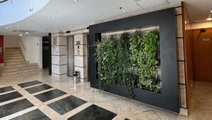 Ένας σύγχρονος χώρος υποδοχής με γεωμετρικά σχέδια στο δάπεδο, έναν κάθετο κήπο και μια σκάλα που οδηγεί σε ανώτερο επίπεδο.
