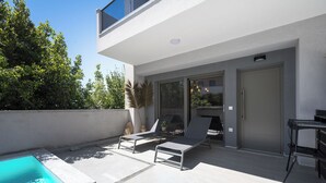 Un patio exterior moderno con piscina, sillas de descanso y zona de barbacoa.