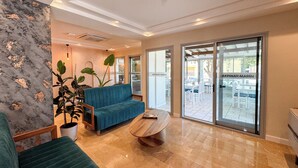 A modern interior with a blue sofa, a wooden coffee table, and a large potted plant. - AKPINAR MARIN OTEL (Cesme)