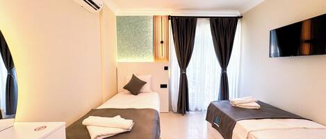 A hotel room with two beds, a flat-screen TV, an air conditioning unit, and a window with curtains.