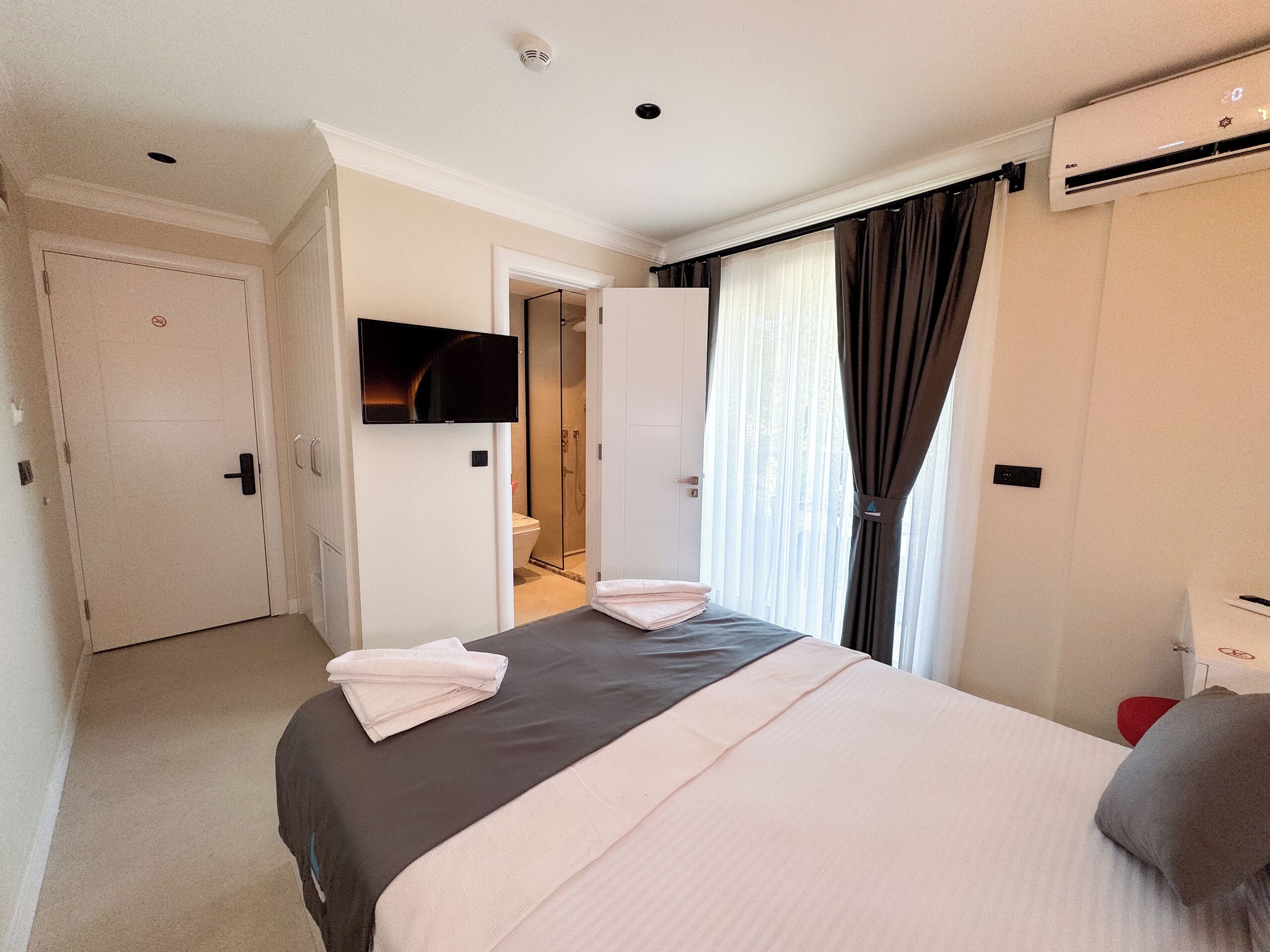 A hotel room with a bed, a TV, a shower, and a window with curtains.
