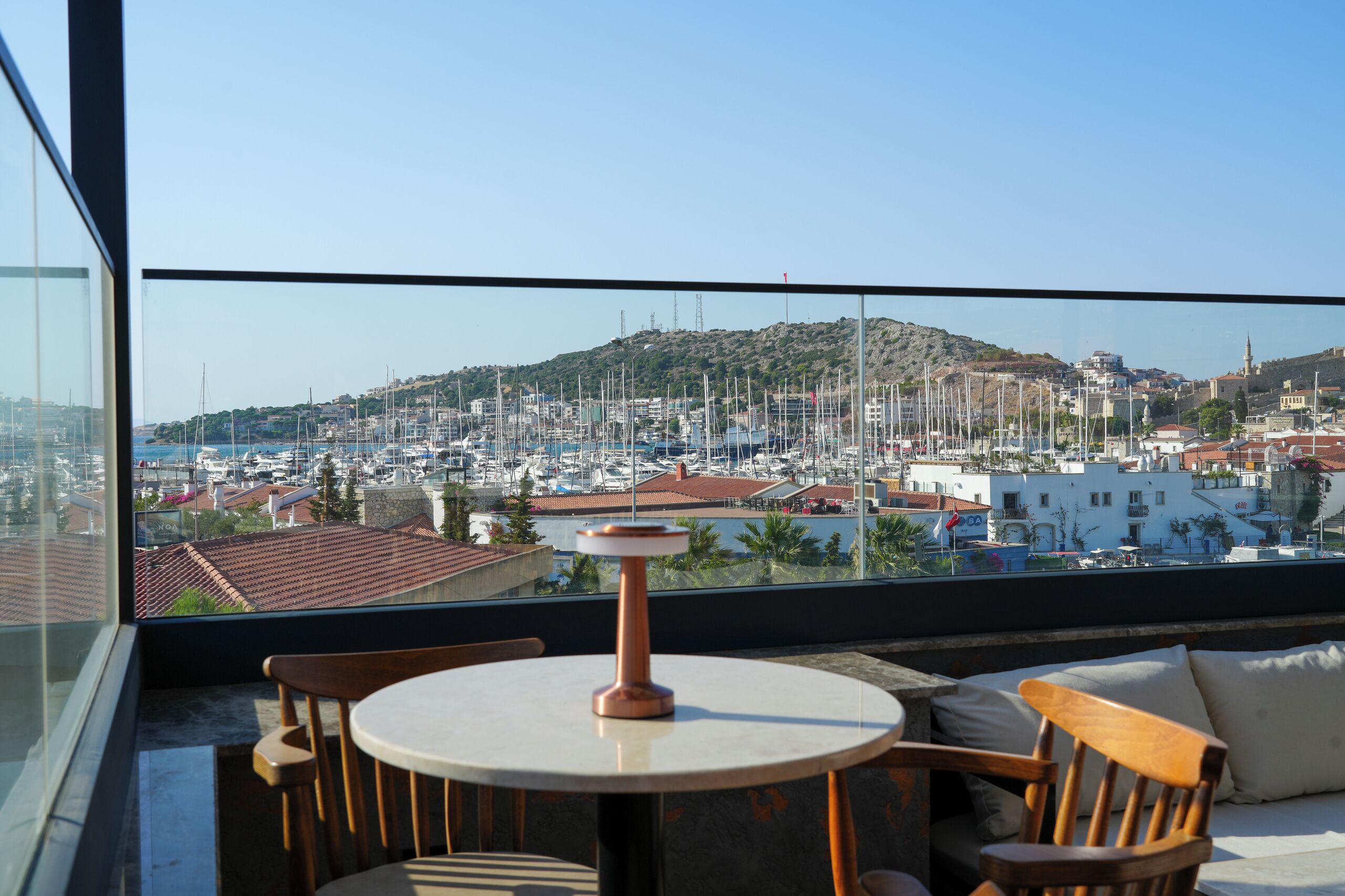 Un balcon avec une table et des chaises, donnant sur une marina où l’on peut admirer des bateaux et des bâtiments.