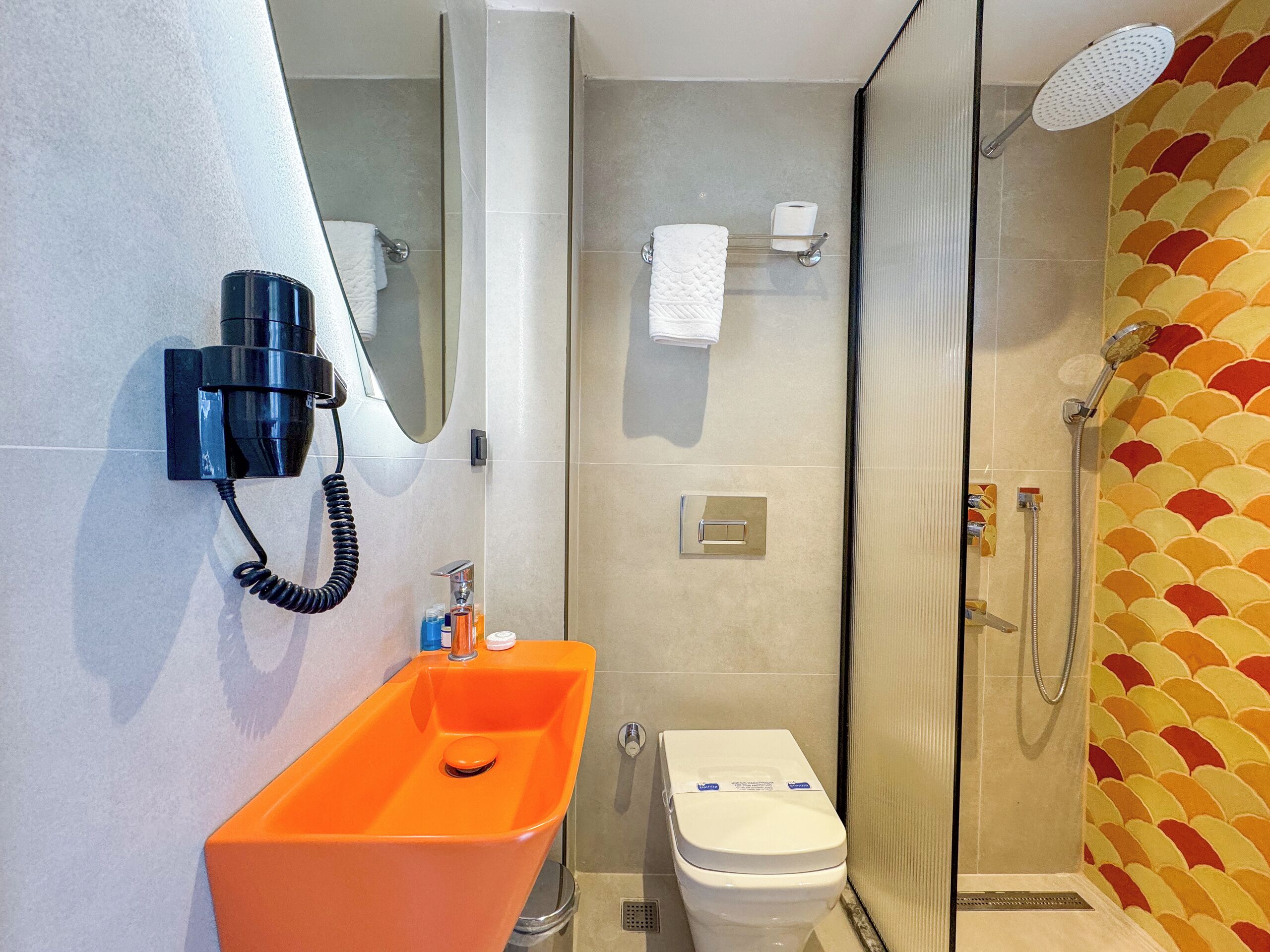 Un bany modern amb una cabina de dutxa de vidre, un vàter blanc i un lavabo taronja.