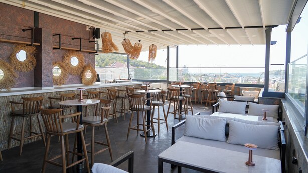 A rooftop restaurant with wooden chairs and tables, large windows, and a view of the city. - AKPINAR MARIN OTEL (Cesme)